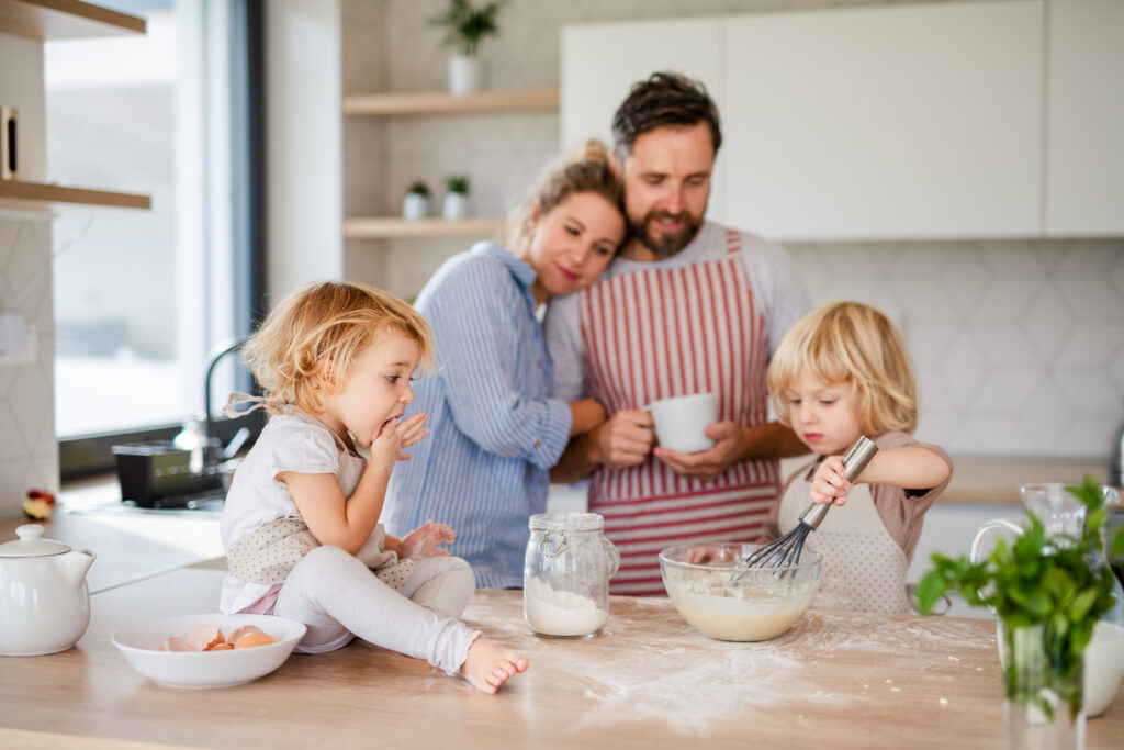 young family with two small children indoors in kitchen, cooking.